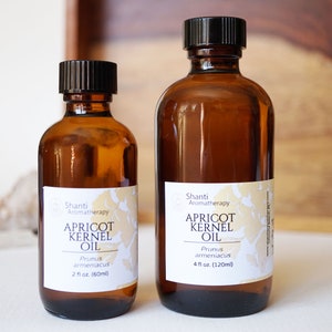 May include: Two amber glass bottles of apricot kernel oil, labeled "Shanti Aromatherapy Apricot Kernel Oil" with the Latin name "Prunus armeniaca" and the volume in fluid ounces and milliliters. The smaller bottle is 2 fluid ounces (60 ml) and the larger bottle is 4 fluid ounces (120 ml).
