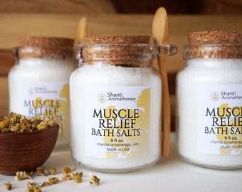 May include: Three glass jars with cork lids filled with white bath salts. The jars have labels that read "Shanti Aromatherapy Muscle Relief Bath Salts 9 fl oz. shantiaromatherapy.com Made in USA".