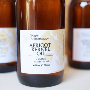 May include: A brown glass bottle with a white label that reads "Shanti Aromatherapy Apricot Kernel Oil Prunus armeniacus 4 fl oz. (120ml)"