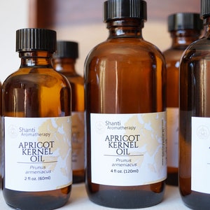 May include: Five amber glass bottles of apricot kernel oil, each with a white label that reads "Shanti Aromatherapy Apricot Kernel Oil Prunus armeniacaus" and the size of the bottle in fluid ounces.