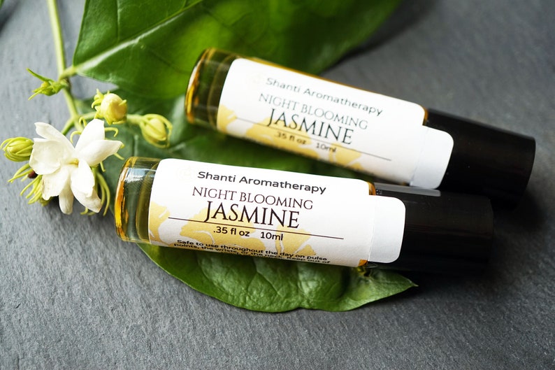 May include: Two small glass bottles with white labels that read "Shanti Aromatherapy Night Blooming Jasmine .35 fl oz 10ml". The bottles are on a gray surface with a green leaf.