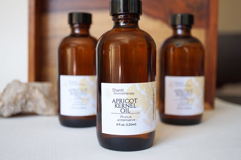 May include: Three amber glass bottles with black caps and white labels. The center bottle label reads "Shanti Aromatherapy Apricot Kernel Oil Prunus armeniaca 4 fl oz (120ml)"