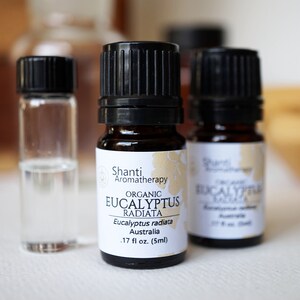 May include: Three small glass bottles with black caps. The center bottle is labeled "Shanti Aromatherapy Organic Eucalyptus Radiata Eucalyptus radiata Australia .17 fl oz. (5ml)"