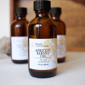 May include: A brown glass bottle with a white label that reads "Shanti Aromatherapy Apricot Kernel Oil Prunus armeniaca 2 fl oz (60ml)".