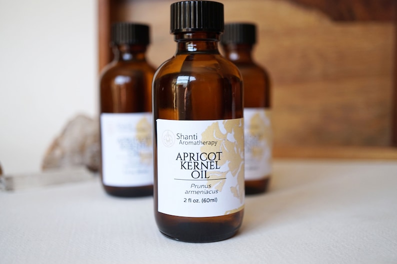 May include: A brown glass bottle with a white label that reads "Shanti Aromatherapy Apricot Kernel Oil Prunus armeniaca 2 fl oz (60ml)".
