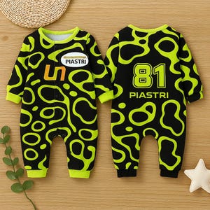 Könnte beinhalten: Ein schwarzer und neongrüner Baby-Overall mit einem einzigartigen Muster. Auf der Vorderseite befindet sich die orangefarbene Zahl "5" und ein "PIASTRI"-Logo. Auf der Rückseite sind die Zahl "81" und der Name "PIASTRI" zu sehen. Der Overall hat lange Ärmel und einen runden Halsausschnitt.
