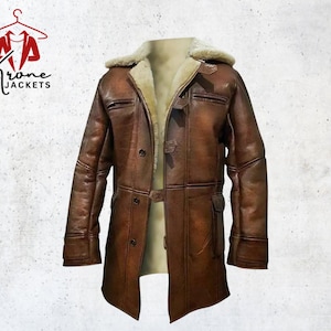 May include: A brown leather jacket with a shearling collar and lining. The jacket has a button-up front, pockets, and a belt detail. The logo "Krone Jackets" is in the upper left corner.