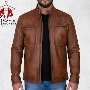 Könnte beinhalten: Braune Lederjacke mit Reißverschluss und zwei Brusttaschen. Die Jacke hat einen Stehkragen und wird über einem schwarzen Hemd getragen. Der Markenname "Krone Jackets" ist oben links sichtbar.