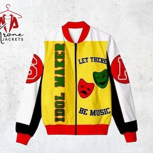 Puede incluir: Chaqueta bomber amarilla, blanca y roja con el texto "IDOL MAKER" y "LET THERE BE MUSIC". La chaqueta tiene cuello, puños y ribetes rojos, con los números "1" y "3" en las mangas. La chaqueta tiene cierre de cremallera.