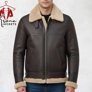 May include: A brown leather jacket with a beige shearling collar and trim. The jacket has a zipper closure and two front pockets. The brand name "Krone Jackets" is visible in the upper left corner.
