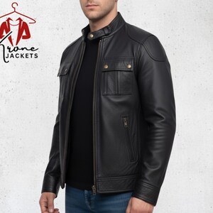 K&ouml;nnte beinhalten: Schwarze Lederjacke mit Stehkragen, zwei Brusttaschen und Rei&szlig;verschluss. Die Jacke wird &uuml;ber einem schwarzen Shirt und blauen Jeans getragen. Das Logo "Krone Jackets" ist sichtbar. Klassisches und zeitloses Design.