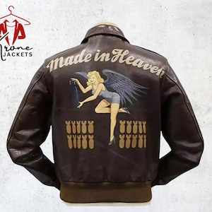 Puede incluir: Chaqueta bomber de cuero marr&oacute;n con un dise&ntilde;o "Made in Heaven" en la espalda. El dise&ntilde;o presenta a una mujer rubia con alas sosteniendo una bomba, con filas de bombas debajo. La chaqueta tiene cuello y pu&ntilde;os marrones.