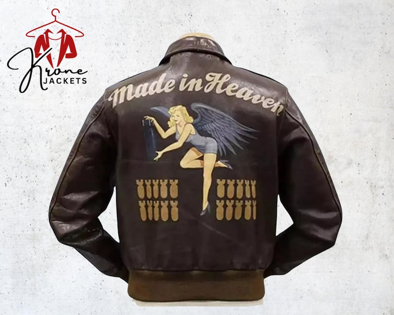 Puede incluir: Chaqueta bomber de cuero marr&oacute;n con un dise&ntilde;o "Made in Heaven" en la espalda. El dise&ntilde;o presenta a una mujer rubia con alas sosteniendo una bomba, con filas de bombas debajo. La chaqueta tiene cuello y pu&ntilde;os marrones.