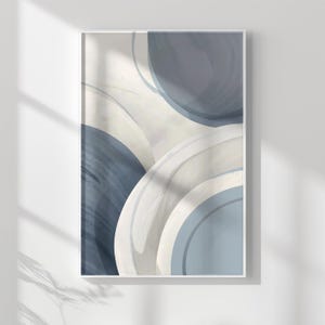 Pode incluir: Impressão de arte abstrata emoldurada com círculos de aquarela sobrepostos em tons de azul e branco sujo. A obra de arte tem uma moldura branca, criando uma estética moderna e minimalista. A composição inclui pinceladas suaves e desfocadas.