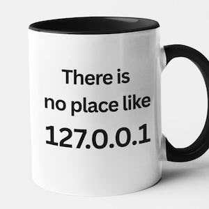 Peut inclure: Mug en céramique blanche avec intérieur, anse et bord noirs. Le mug affiche le texte "There is no place like 127.0.0.1" en noir, une référence humoristique au localhost d'un ordinateur.