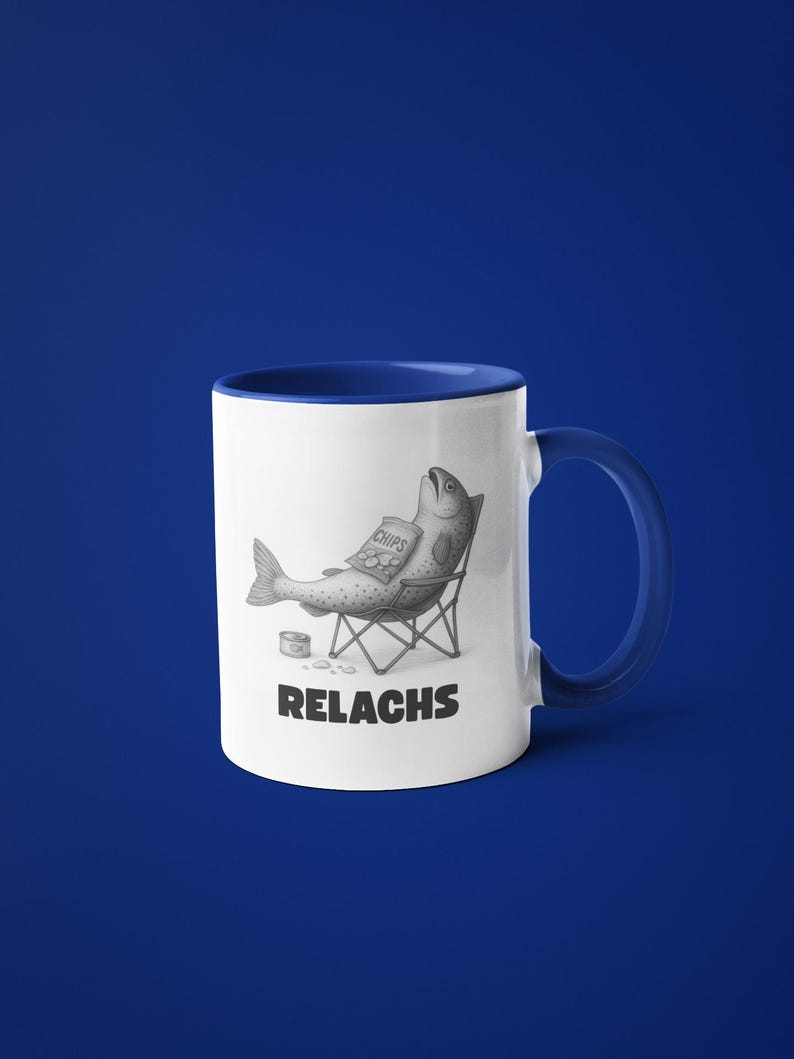 May include: White ceramic mug with a blue interior and handle. The mug features a humorous illustration of a fish relaxing in a folding chair, holding a bag of chips. The word "RELACHS" is printed below the image.