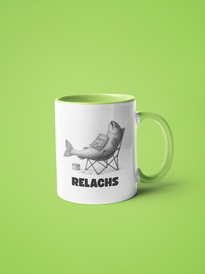 May include: White ceramic mug with a green handle and interior. The mug features a humorous illustration of a fish relaxing in a beach chair, holding a bag of chips. The word "RELACHS" is printed below the illustration.