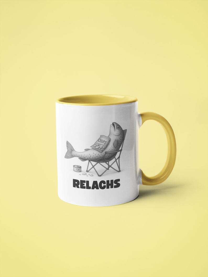 May include: White ceramic mug with a yellow interior and handle. The mug features a black and white illustration of a fish relaxing in a beach chair, holding a bag of chips. The word "RELACHS" is printed below the illustration.