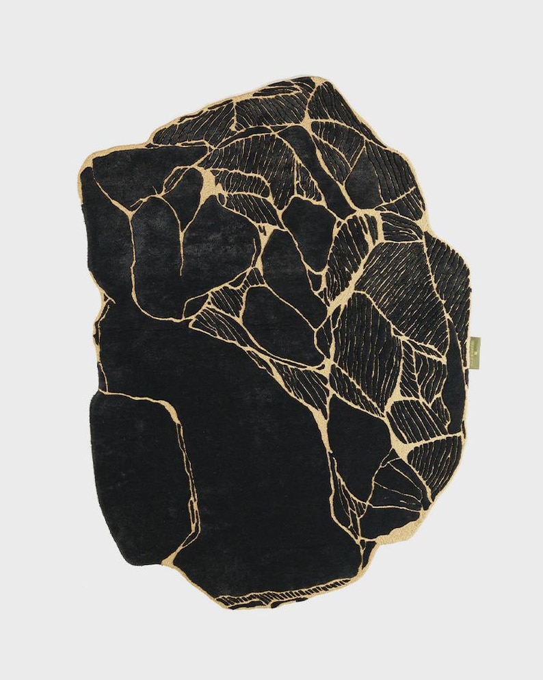 May include: A black rug with a unique, organic shape. The rug features a striking design of interconnected, gold-colored lines against a solid black background. The overall aesthetic is modern and artistic, suitable for various interior styles.