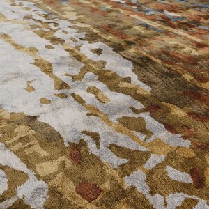 May include: Abstract area rug with a blend of colors. The rug features a light gray base with brown, gold, and rust-colored accents. The design includes vertical and diagonal patterns, creating a textured appearance.