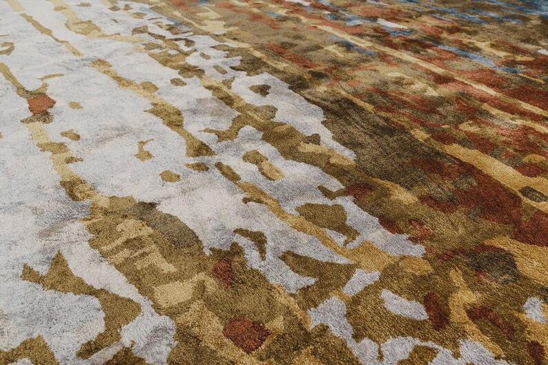 May include: Abstract area rug with a blend of colors. The rug features a light gray base with brown, gold, and rust-colored accents. The design includes vertical and diagonal patterns, creating a textured appearance.