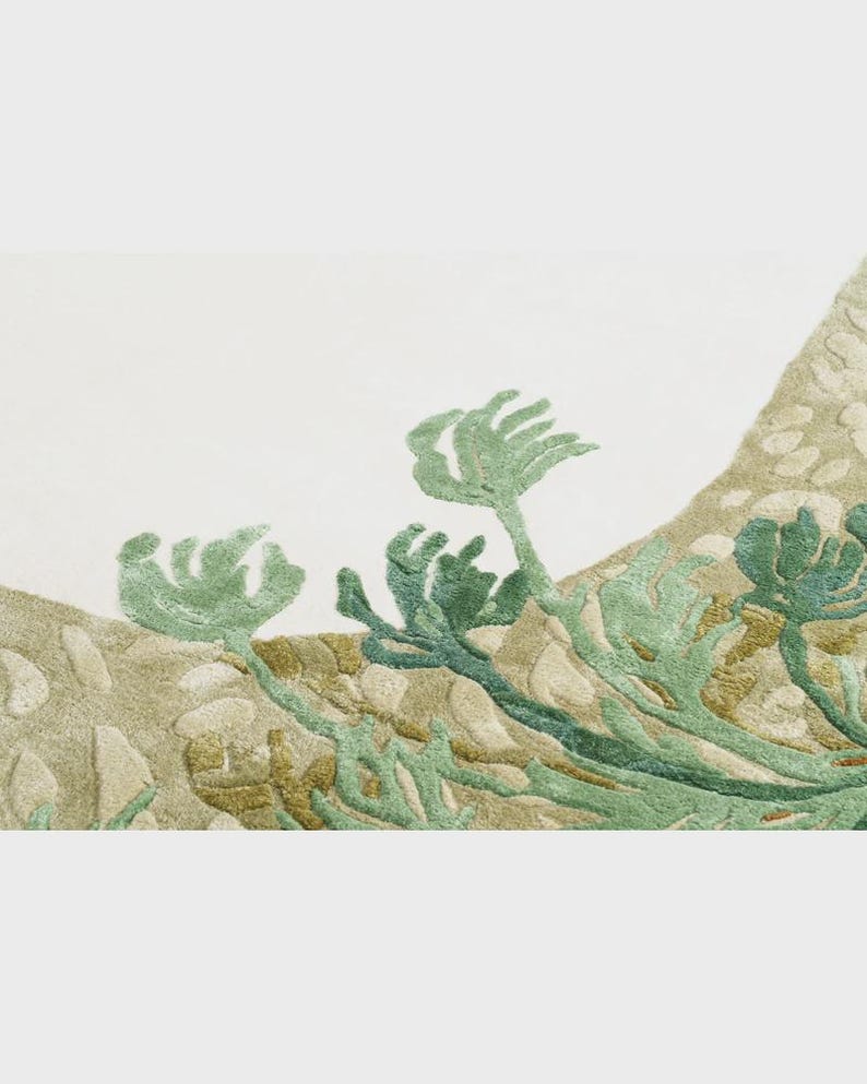 May include: Close-up of a textile with an embroidered design featuring green and blue-green plant-like forms against a beige and off-white background. The design has a textured, three-dimensional appearance, suggesting a rug or wall hanging.