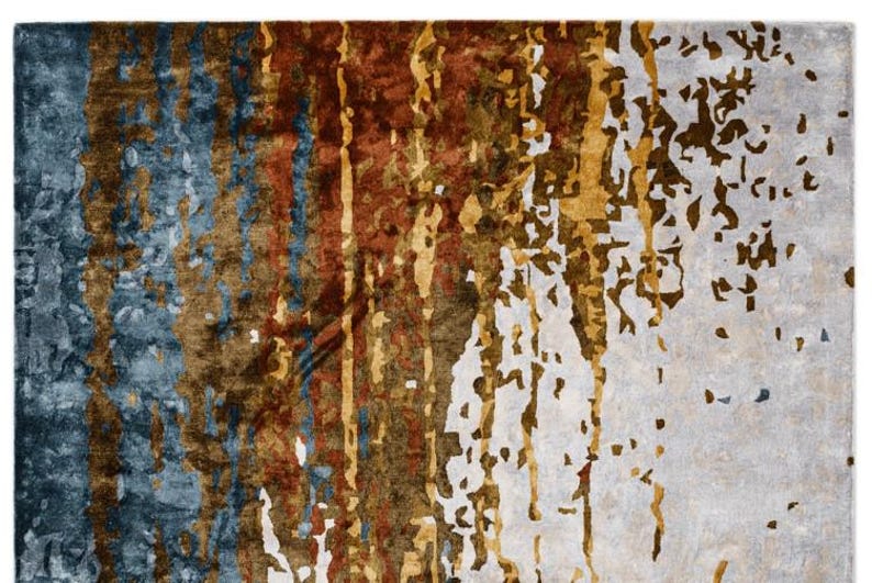 May include: Abstract area rug with a distressed design. The rug features a blend of colors, including blue, brown, gold, and white, creating a textured, artistic appearance. The design has vertical and scattered elements.