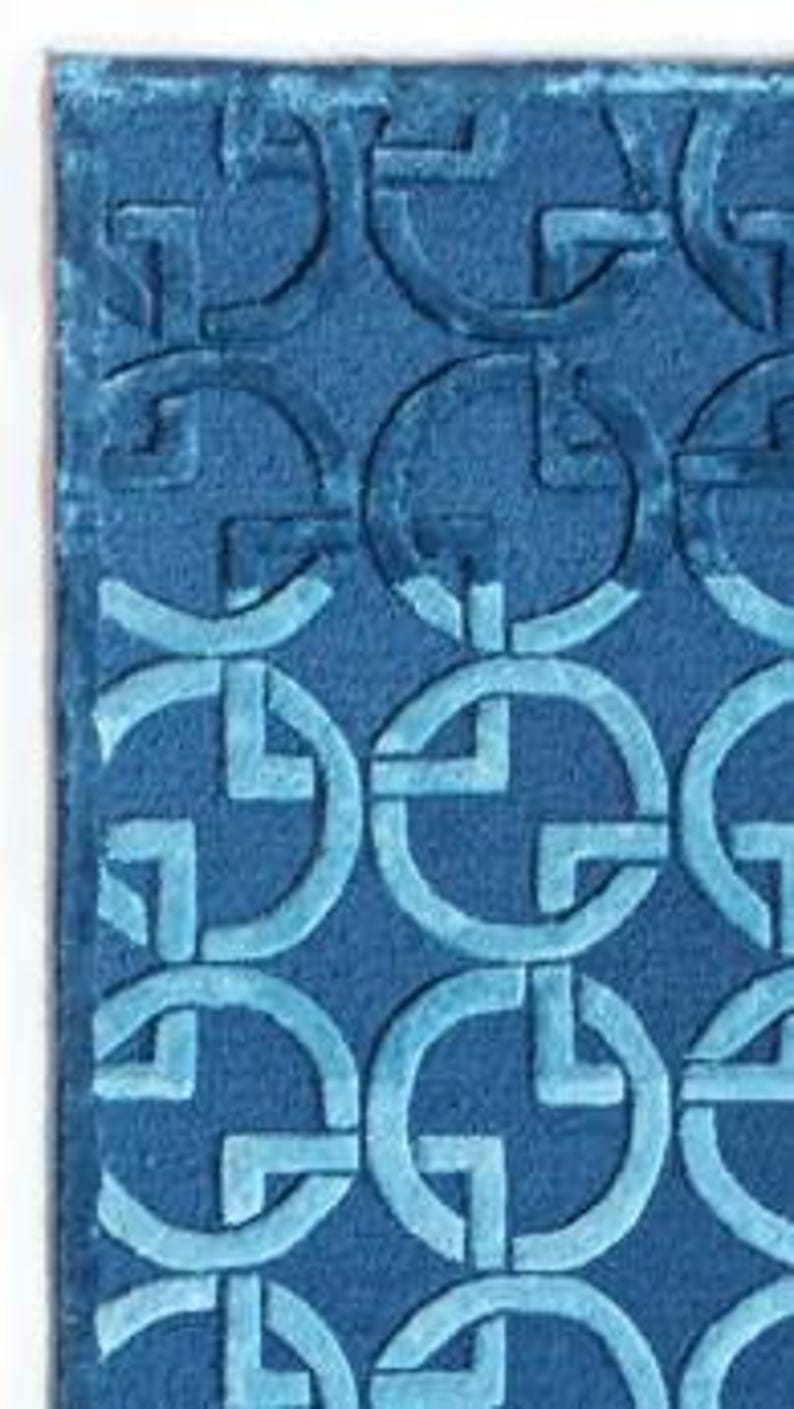 May include: A rectangular blue rug with a repeating pattern of interlocking circles and squares. The design is a lighter shade of blue than the rug's background. The rug has a soft, textured appearance.