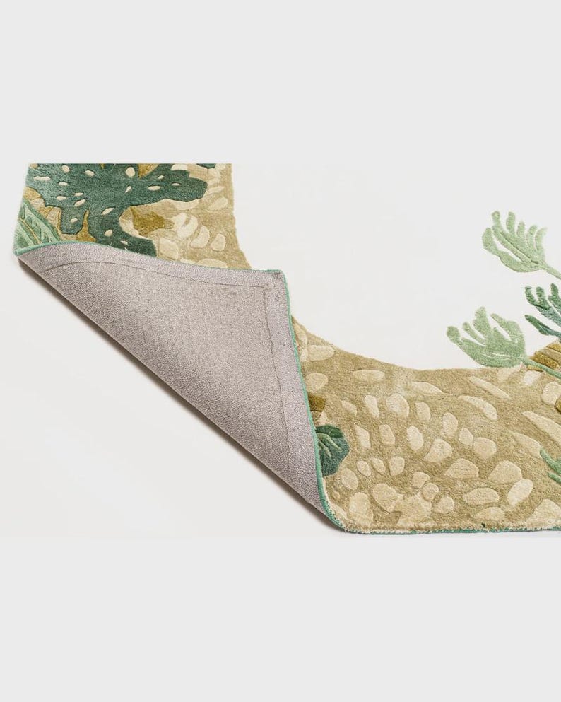 May include: A section of a decorative rug with a botanical design. The rug features a beige background with green and olive-colored floral patterns. The underside of the rug is visible, showing a gray backing and a green border.