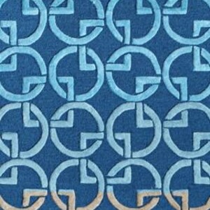 May include: A blue rug with a repeating pattern of interlocking circles and cross-like shapes. The design features varying shades of blue and a touch of beige, creating a textured, geometric aesthetic. The rug's design is suitable for home decor.