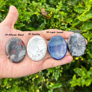 May include: Four polished gemstone ovals: African Blood, Howlite, Lapis Lazuli, and Larvikite. The African Blood stone is gray with red inclusions. Howlite is white with gray veining. Lapis Lazuli is blue. Larvikite is gray with black inclusions.