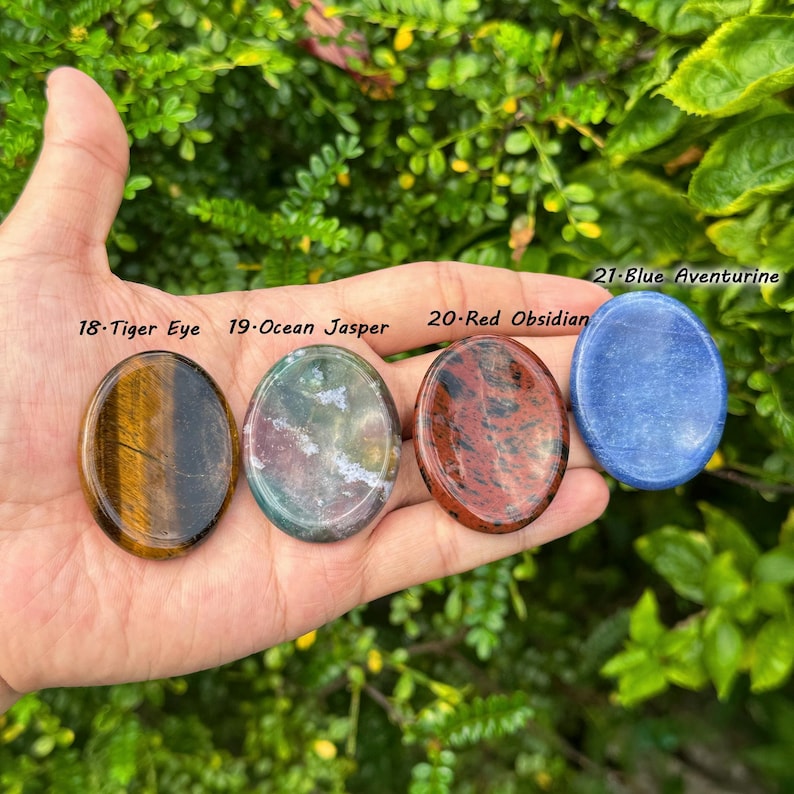 May include: Four polished gemstones: Tiger Eye, Ocean Jasper, Red Obsidian, and Blue Aventurine. The Tiger Eye is brown with gold streaks. Ocean Jasper is green and white. Red Obsidian is red with black patterns. Blue Aventurine is a solid blue color.