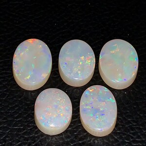 以下が含まれることがあります： 乳白色のベースと虹色の色のきらめきを持つ5つの楕円形のオパール。 オパールは、赤、緑、青の色合いで、色の遊び効果を示しています。 宝石は暗い背景にあります。