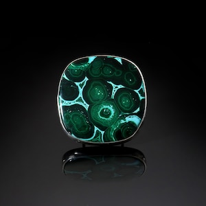 May include: A green and white malachite stone set in a silver ring. The stone has a unique pattern of concentric circles.