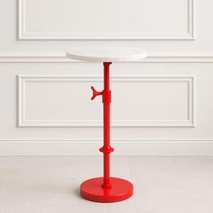 Könnte beinhalten: Ein roter, verstellbarer Beistelltisch mit einer runden, weißen Tischplatte. Der Tisch hat einen roten Sockel und eine rote Mittelsäule mit einem Verstellhebel. Der Tisch ist für den Innenbereich konzipiert.