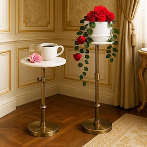 Puede incluir: Dos mesas auxiliares de altura ajustable con tapas de mármol y bases de latón. Una mesa tiene una taza blanca y un vaso de agua, con una rosa rosa. La otra muestra una maceta blanca con rosas rojas y follaje verde.