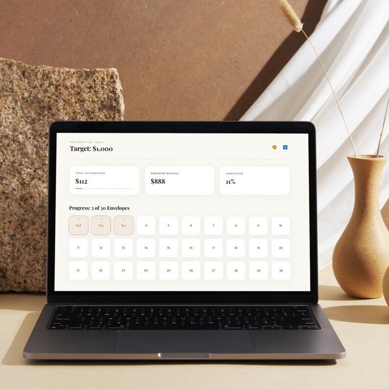 May include: A laptop displaying a savings tracker with the text "Target: $1,000". The screen shows "$112" accumulated, "$888" remaining, and 11% completion. The progress bar indicates 1 of 30 envelopes.