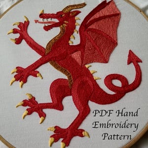 May include: Hand-embroidered red dragon design on white fabric, stretched within a wooden embroidery hoop. The dragon features gold accents on its horns, claws, and body. The text "PDF Hand Embroidery Pattern" is visible.