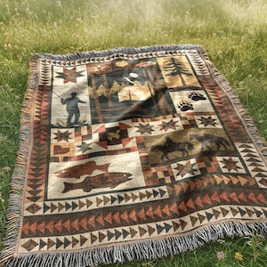 May include: A rectangular woven throw blanket with a nature-themed design. The blanket features images of fish, bears, trees, and a fisherman. The color palette includes shades of brown, beige, and green, with a fringed edge. The blanket is placed on a grassy surface.