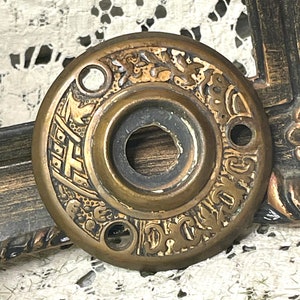 May include: A brass door knob escutcheon with an ornate design and the text "D.C.G. 2010" around the edge.