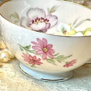 May include: A white teacup with a gold rim and floral pattern. The pattern features pink and yellow flowers with green leaves.