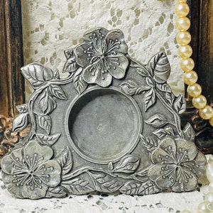 May include: A silver metal trinket dish with a floral design. The dish has a round center and is surrounded by leaves and flowers.