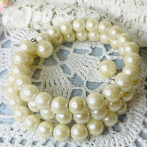 May include: A multi-strand wrap bracelet featuring round, cream-colored faux pearls. The design consists of several continuous loops of beads, each finished with a single pearl at the end of the wire, creating a flexible, coiled structure.