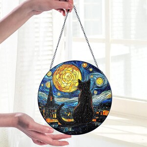 May include: Round stained glass art piece featuring a black cat silhouette gazing at a yellow moon and starry night sky. The artwork is reminiscent of Van Gogh's style, with a chain for hanging. The cat is perched on a rooftop.