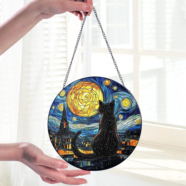 May include: Round stained glass art piece featuring a black cat silhouette gazing at a yellow moon and starry night sky. The artwork is reminiscent of Van Gogh's style, with a chain for hanging. The cat is perched on a rooftop.