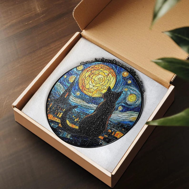 May include: A round, black cat silhouette gazing at a yellow moon and starry night sky, reminiscent of Van Gogh's "Starry Night." The artwork is set in a black frame and presented in a cardboard box with white padding. The cat is perched on a rooftop.
