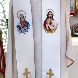 以下が含まれることがあります： クリーム色の宗教的祭服で、刺繍が施されています。 ストールには、十字架、小麦、ブドウなど、宗教的な人物やシンボルの画像が描かれています。 画像は金のアクセントで縁取られています。 祭服は柔らかく流れるような生地で作られています。