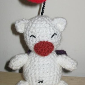 May include: White crocheted stuffed toy with a red nose and purple wings. The toy is holding a red balloon.