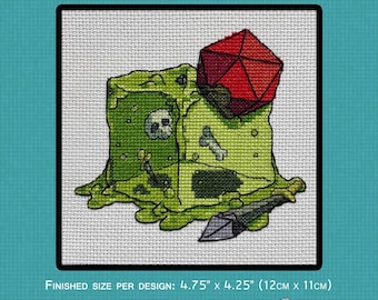May include: Cross-stitch pattern with a green dice cube design, a skull, bone, and sword. A red 20-sided die sits on top. The text "DICE CUBE PATTERN" is at the top. Finished size is 12cm x 11cm.