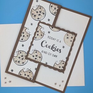 May include: A greeting card with a white background and a brown border. The card features a repeating pattern of chocolate chip cookies and the text "Today is a Cookies kind of day."